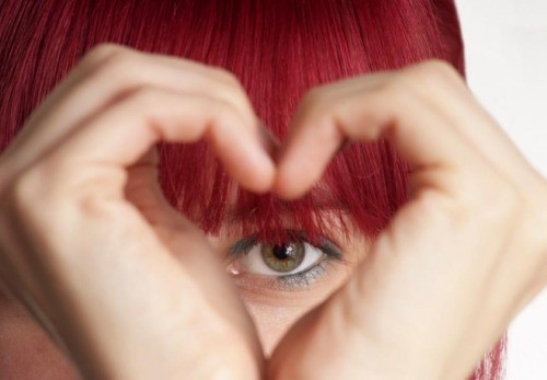 Kvinde med roedt haar lavet et hjerte med haenderne