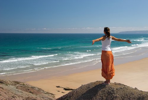Kvinde der staar med spredte arme ved en strand