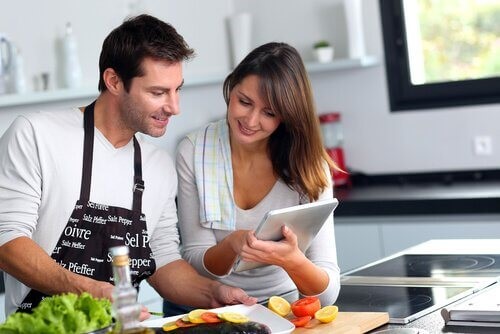 Mand der laver mad, mens hans partner viser ham noget paa en tablet