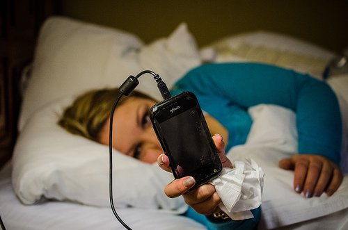 Kvinde der ligger med sin telefon i sengen