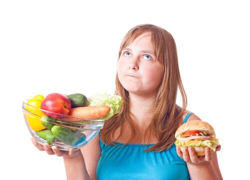 Ung kvinde der staar med groentsager og en burger