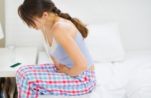 Kvinde der sidder paa sin seng med mavesmerter