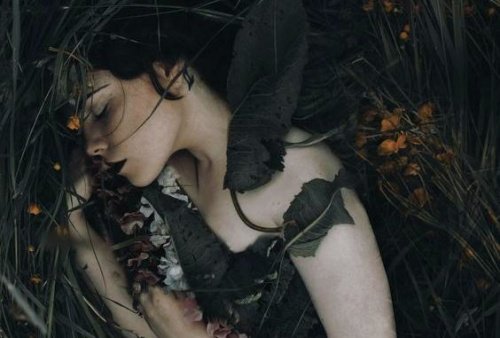 Kvinde der ligger med nogle blade over sig