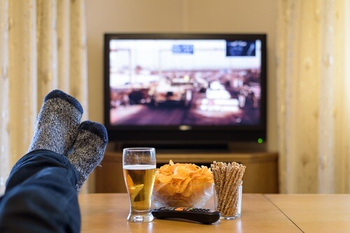 Mand der ser tv med oel og chips