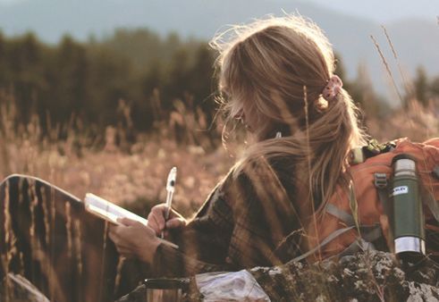 Kvinde der skriver dagbog paa en eng