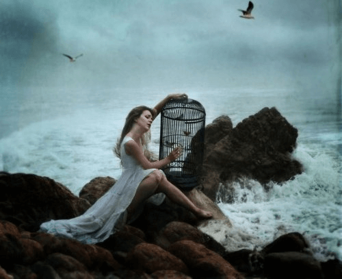 Kvinde med et fuglebur ved vandet