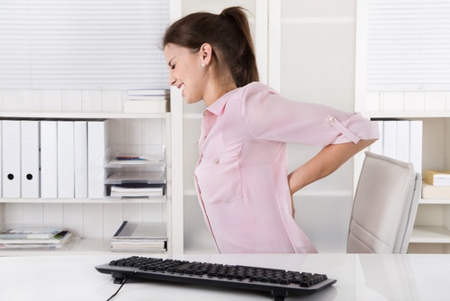 Kvinde der sidder paa kontoret med smerter i ryggen