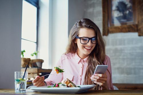Kvinde der sidder med sin mobil mens hun spiser