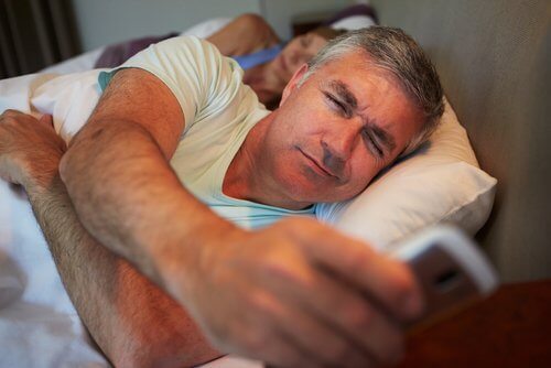 Mand ser på telefon i sengen i stedet for at sove