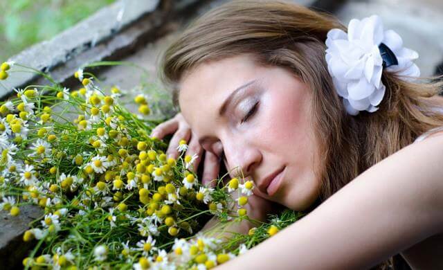 Kvinde der ligger med lukkede oejne ved nogle blomster