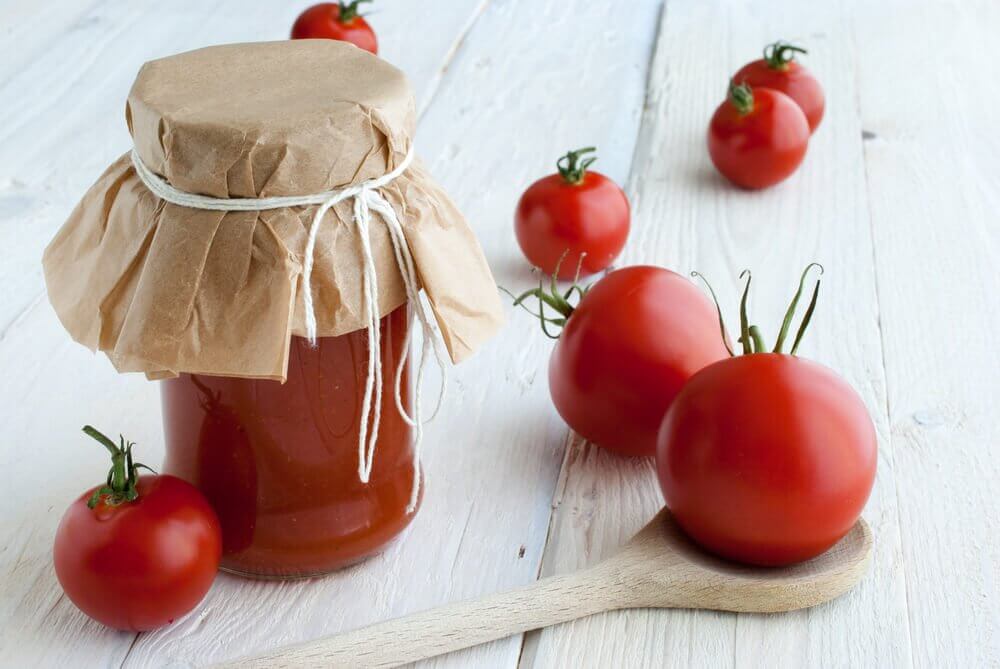 Glaskrukke med tomatsovs ved siden af friske tomater.
