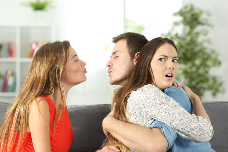 En mand krammer en kvinde, mens han proever at kysse en anden kvinde bag hendes ryg