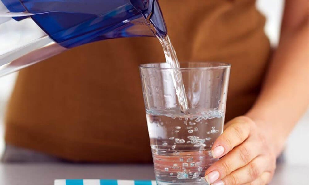 Person hælder vand i glas fra kande.