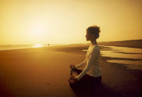 Kvinde der mediterer paa en strand