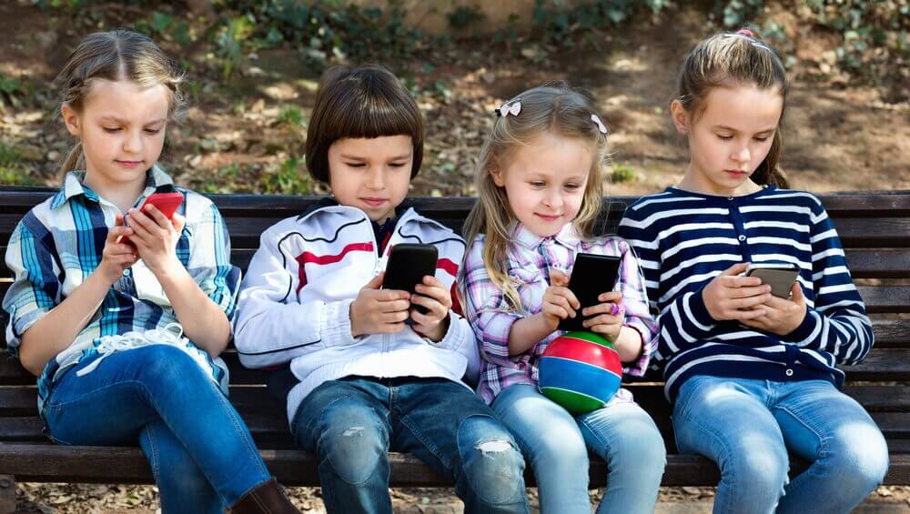 Fire børn på en bænk med deres telefoner