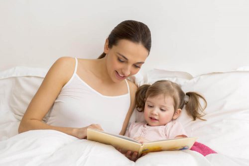 Mor der sidder og laeser med sin datter i sengen