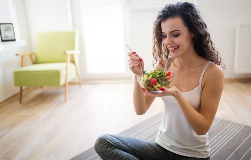 Kvinde spiser salat i stuen