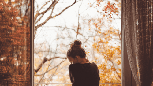Kvinde i vindue foran efterårstræer