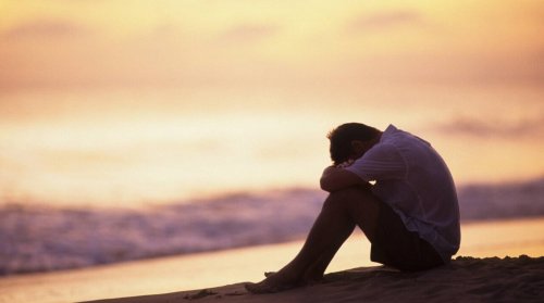 Mand på strand er deprimeret og hviler hoved på knæ