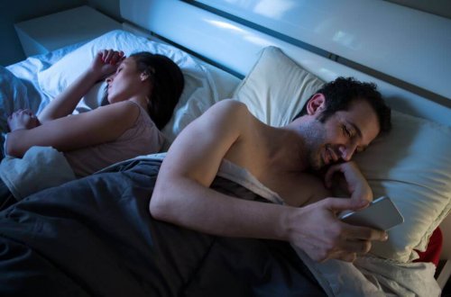 Mand, der ligger og sms'er ved siden af sin partner