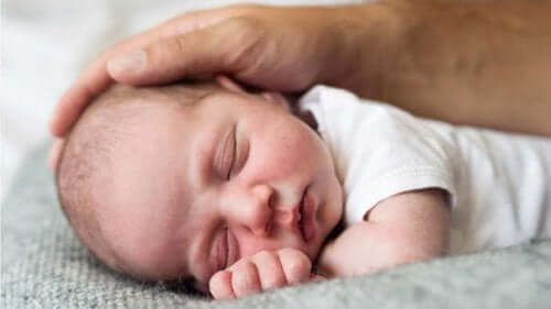 Baby sover med forælders hånd på hoved