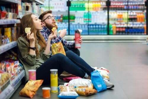 Mand og kvinde sidder i gang i supermarket og spiser chips