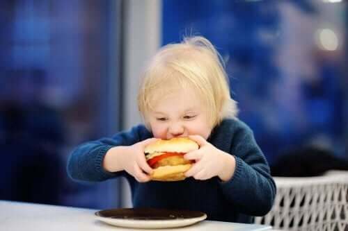 Barn med stor burger symboliserer overvægt i barndommen