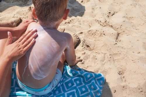 Dreng får smurt solcreme på ryg som del af at pleje børns hud om sommeren