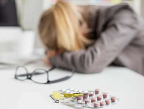 Kvinde med hoved i bord og en pakke piller ved siden af sig