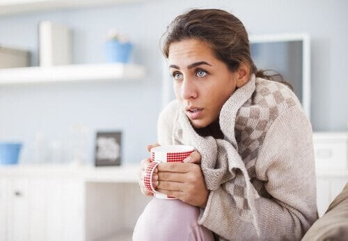 Kvinde forsøger at få varmen med varm te og varmt tøj
