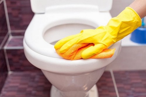 Tips til at rengøre hjemmet under corona-krisen illustreres af person, der skrubber toilet