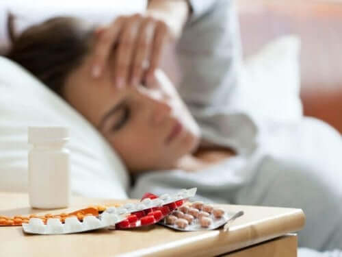 Kvinde med hovedpine og piller på sengebord