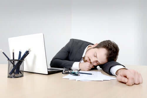 Mand sover på skrivebord som eksempel på de forskellige typer af søvnløshed