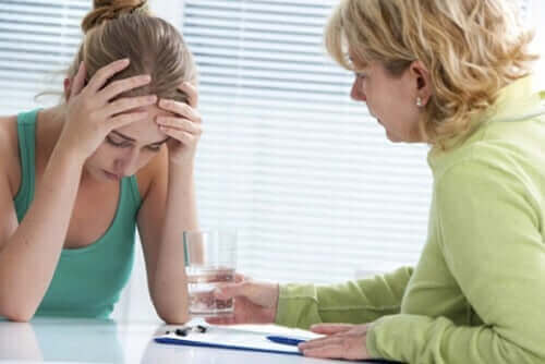 Kvinde tager sig til hoved, mens en anden kvinde rækker hende et glas vand