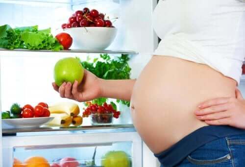 Kost under graviditet illustreres af gravid kvinde ved fyldt køleskab