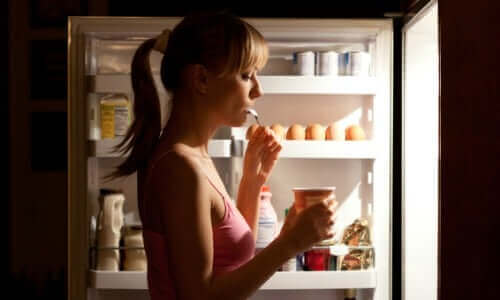Kvinde spiser fra åbent køleskab om aftenen