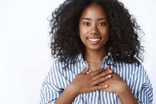 Kvinde, der smiler og tager sig til hjerte, er taknemmelig, hvilket er vejen til lykke ifølge videnskaben