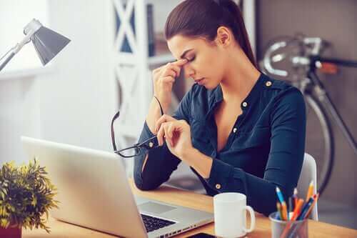 Kvinde ved skrivebord har hovedpine grundet daglig stress