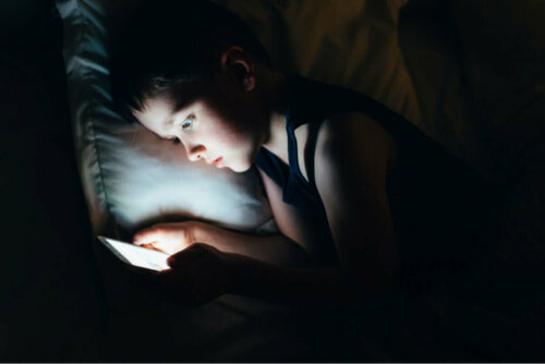 Dreng ligger med telefon i mørke i sengen