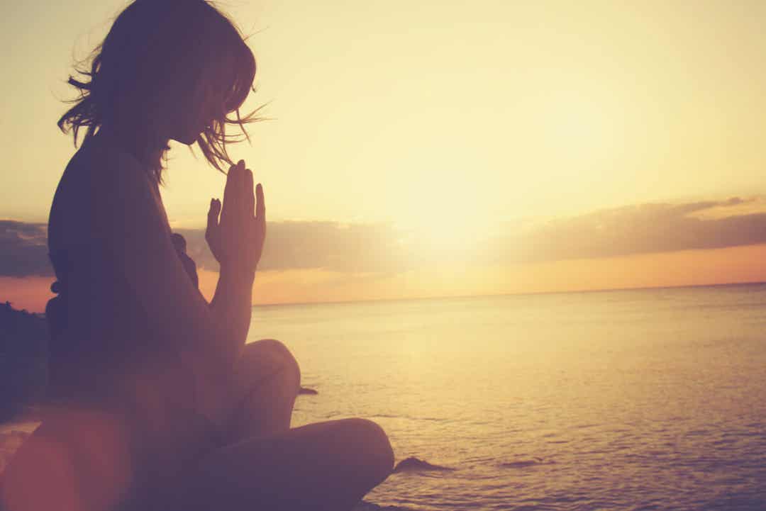 Kvinde mediterer ved vand for at leve mere bevidst