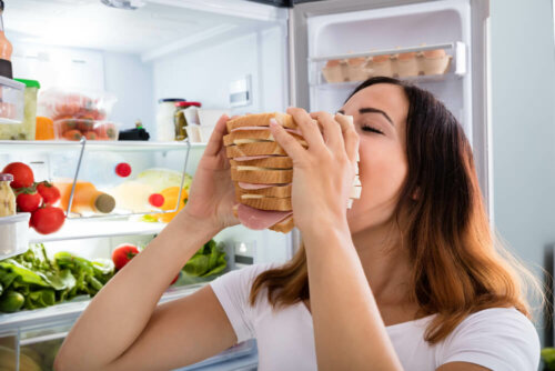 Kvinde foran køleskab spiser en kæmpe sandwich