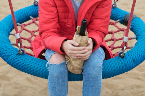 Person på legeplads med vinflaske i hånden