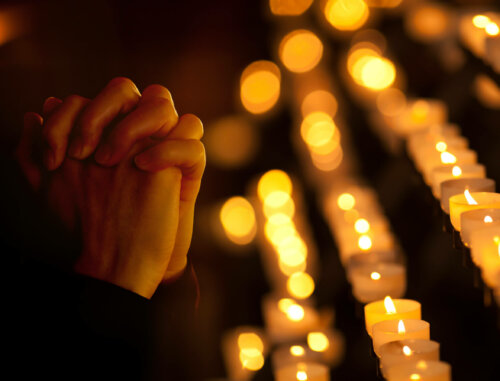 Hænder beder i kirke med stearinlys