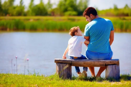 Far og søn sidder sammen ved sø