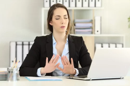 Kvinde ved skrivebord trækker vejret dybt for at undgå fiasko og selvsabotage