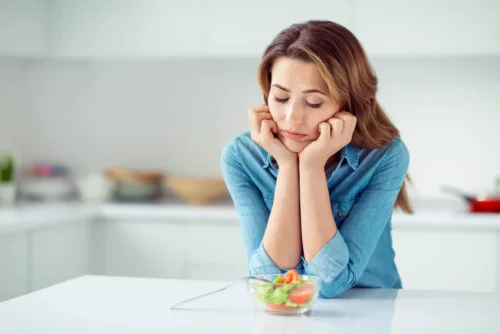 Trist kvinde, der følger 1000-kalorie-diæten, ser på salat