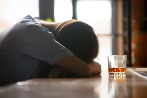 Fuld person med et glas alkohol foran sig hviler hovedet på bordet