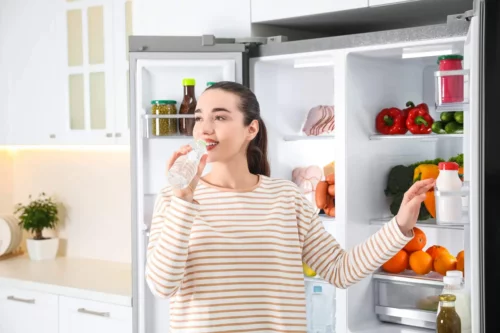 Kvinde drikker vand foran køleskab
