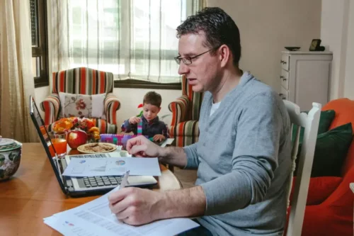 En mand arbjeder hjemmefra og passer sin søn samtidig ved hjælp af multitasking