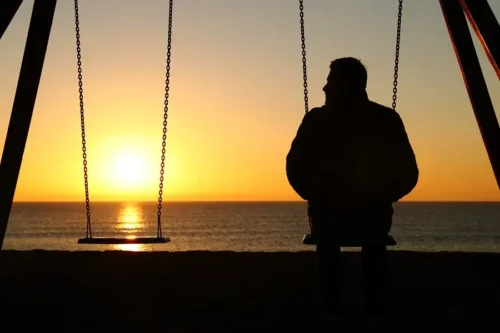 Mand sidder på gynge og ser på solnedgang